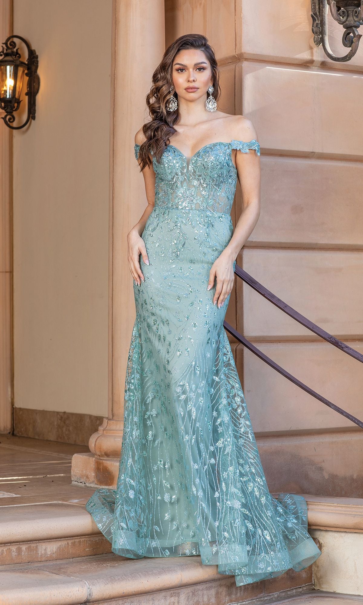 A woman stands on stone steps wearing the Off-the-Shoulder Long Glitter Prom Dress, a fitted light blue gown featuring intricate embellishments and sparkling beaded details.
